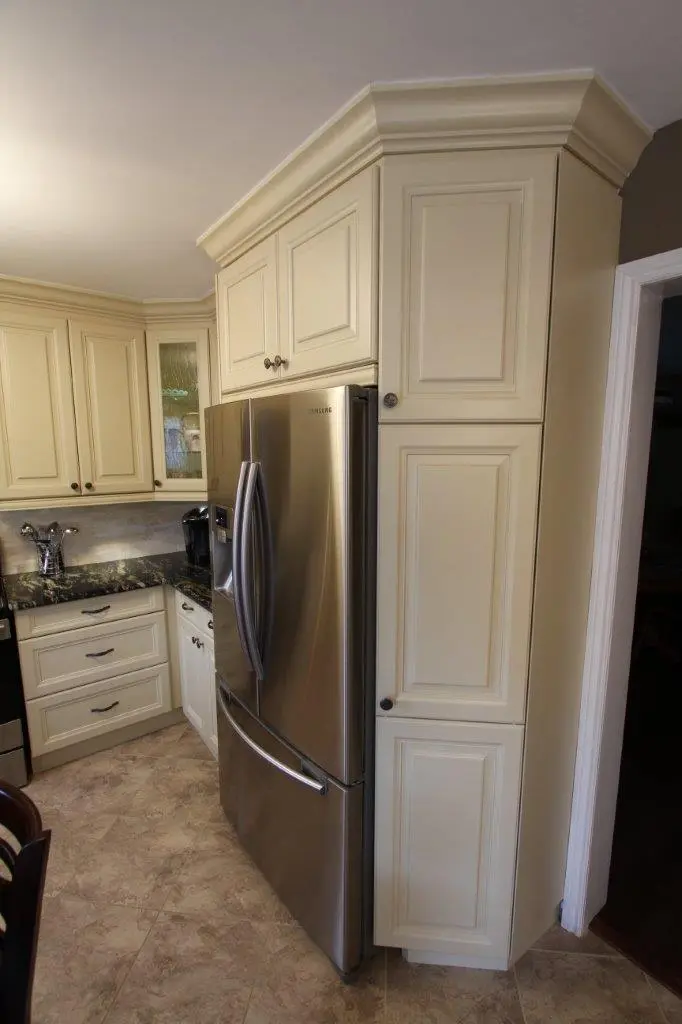 Modern kitchen corner with stainless steel Samsung refrigerator surrounded by cream-colored cabinets, granite countertops, and beige tiled floor.