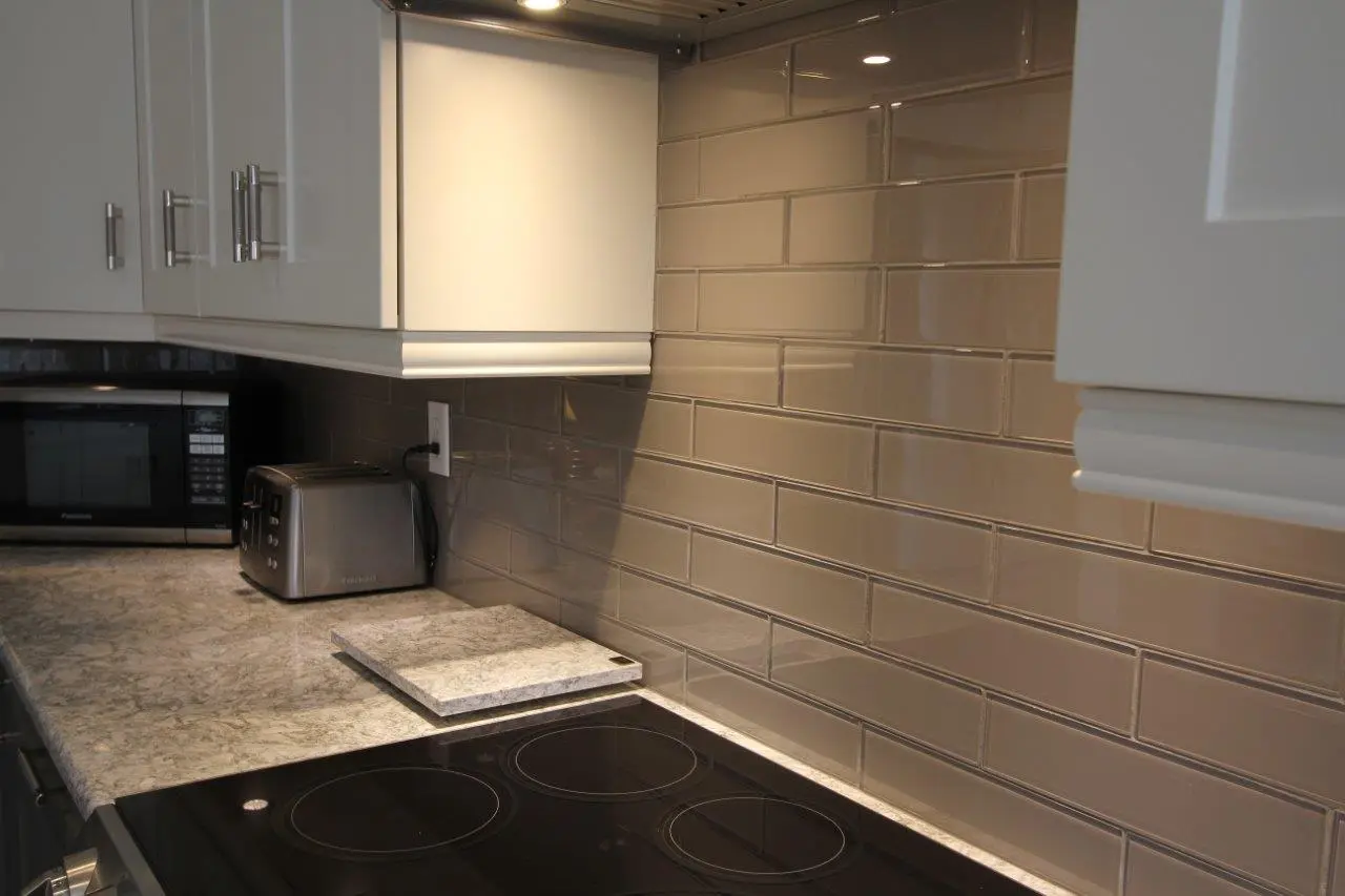 Modern kitchen countertop with a built-in black electric stove, a stainless steel toaster, a microwave, white cabinetry, and a glossy gray subway tile backsplash.