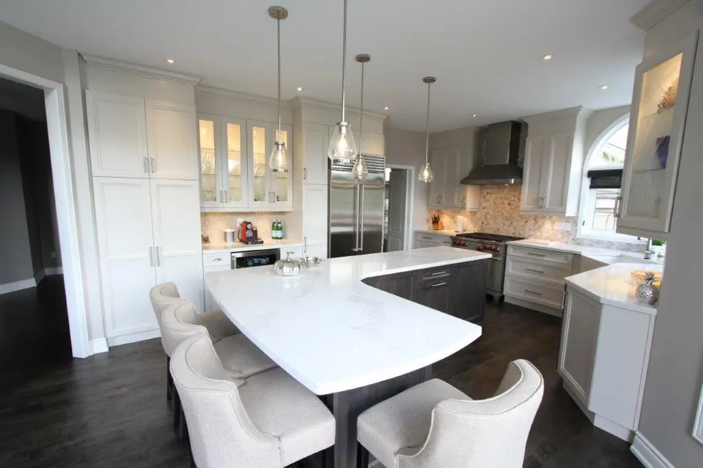 Modern kitchen with white cabinetry, dark wood flooring, a large white marble island with four upholstered chairs, stainless steel appliances, pendant lights, and a window with an arched top.
