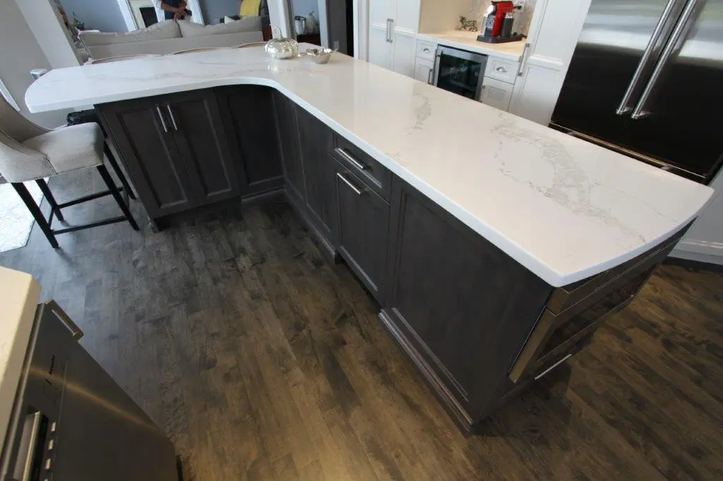 Modern kitchen island with dark wood cabinets and a white marble countertop, set on dark wood flooring, with a light gray upholstered bar stool nearby and stainless steel appliances around.