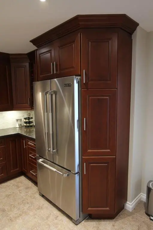 Modern kitchen corner featuring a stainless steel French door refrigerator surrounded by dark wood cabinetry with silver handles on a tiled floor.