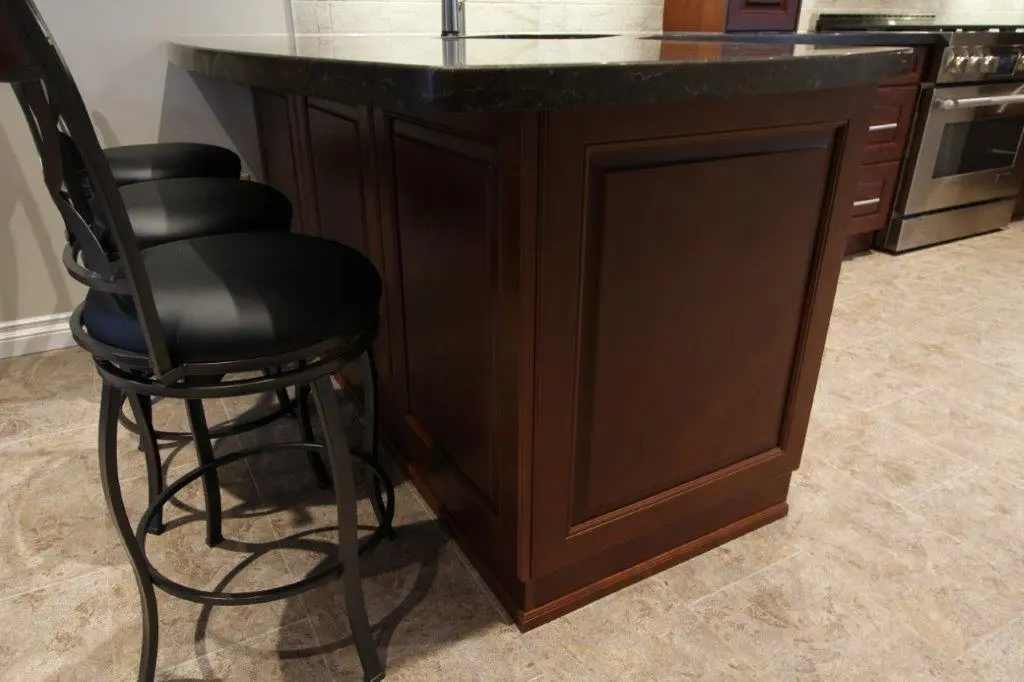 Two black cushioned bar stools with metal frames next to a dark wooden kitchen island with a black countertop on a tiled floor.