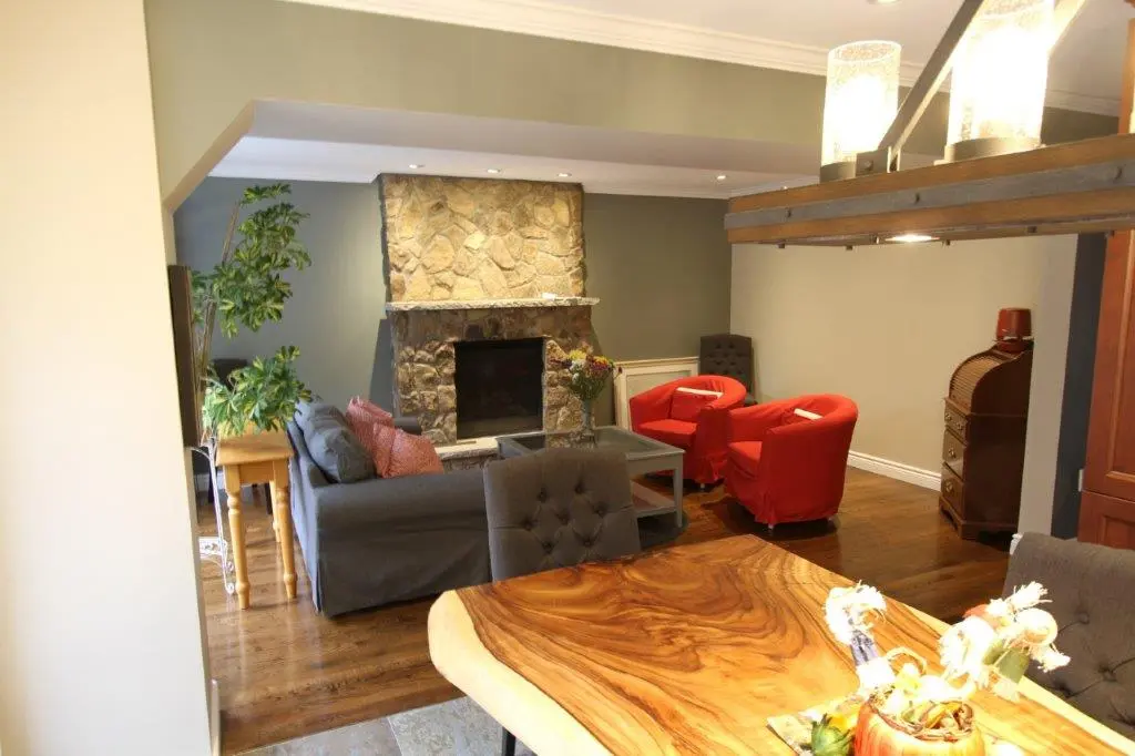 Living room featuring a stone fireplace, a gray couch with pink cushions, two red armchairs, a wooden table with a natural edge in the foreground, and a small side table with a green plant.