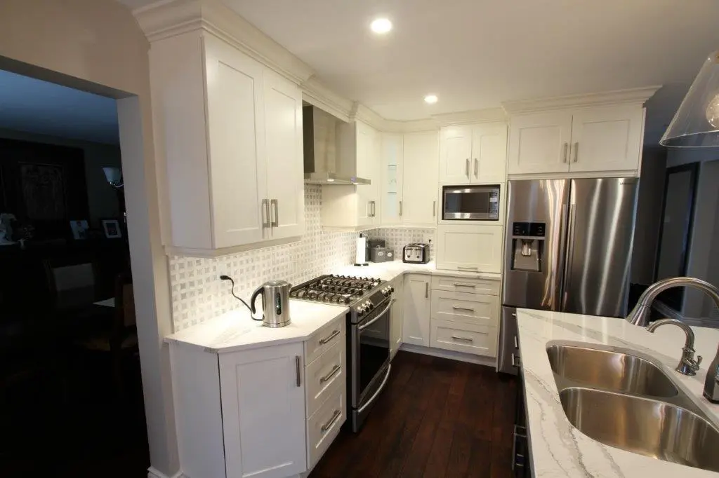 Modern kitchen with white cabinets, a stainless steel gas stove, microwave, and refrigerator, white marble countertops, a stainless steel double sink, and dark wooden flooring.