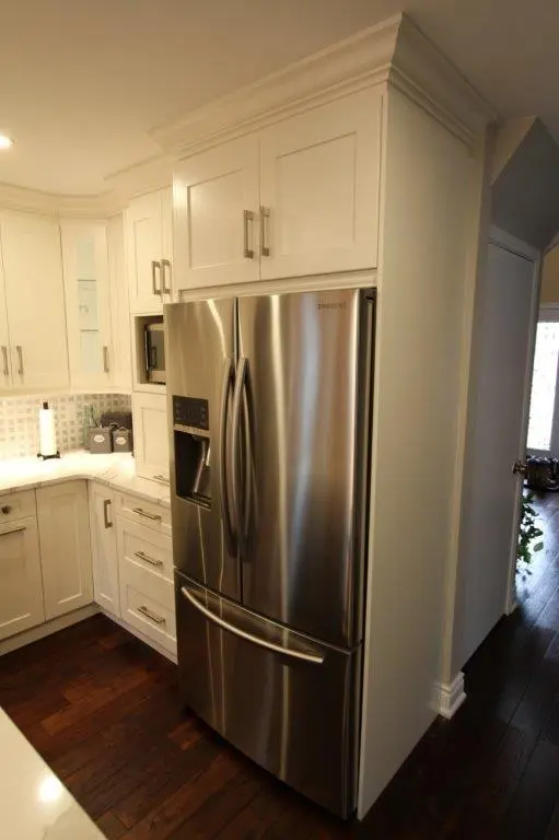 Stainless steel Samsung French door refrigerator integrated into white kitchen cabinetry with dark wood flooring and white countertops.