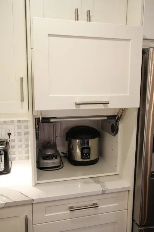 White kitchen cabinet with an open upward-hinged door revealing a blender and a rice cooker inside.