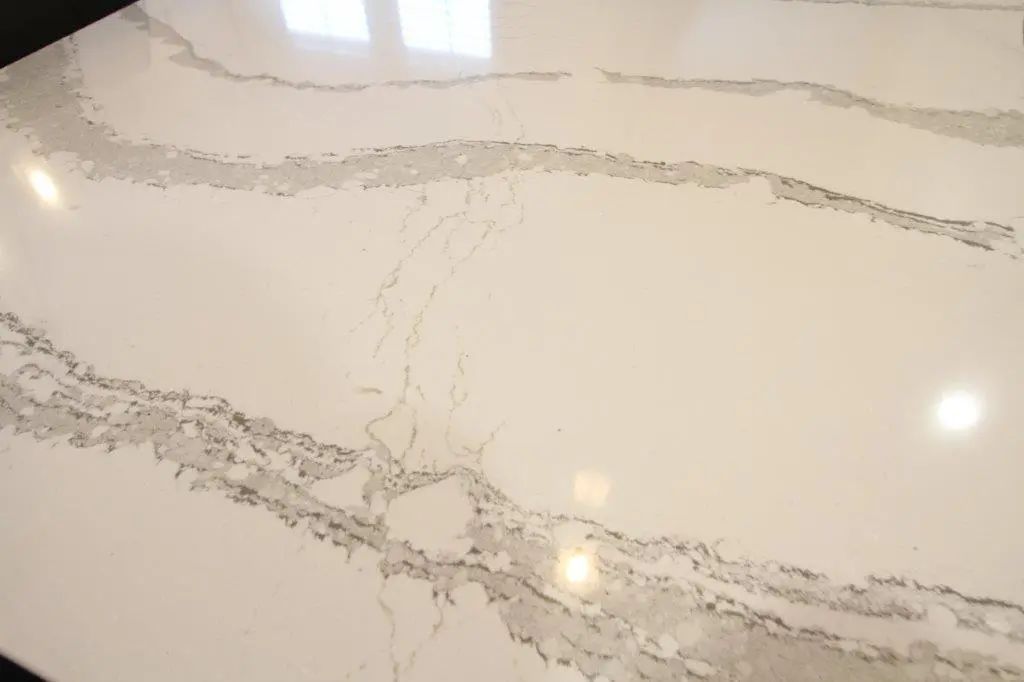 Close-up of a smooth, polished white marble surface with grey veining and reflections of lights and window patterns.