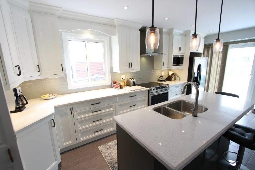 Modern kitchen with white cabinets, a large island with a double sink and chrome faucet, stainless steel appliances, three pendant lights, and a window above the countertop letting in natural light