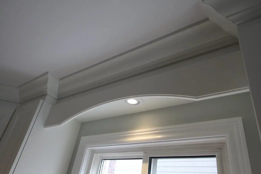 White ceiling with crown molding and a recessed light above a window with white trim.