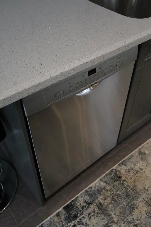 Stainless steel Bosch dishwasher integrated under a light gray speckled countertop in a modern kitchen setting.