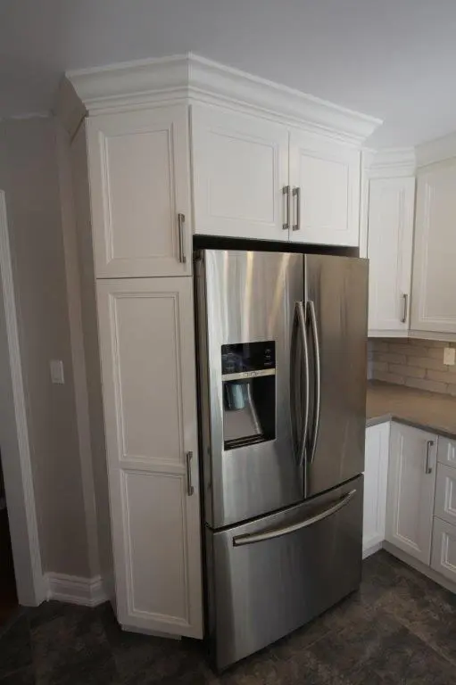 Stainless steel French door refrigerator with water dispenser built into white kitchen cabinetry.