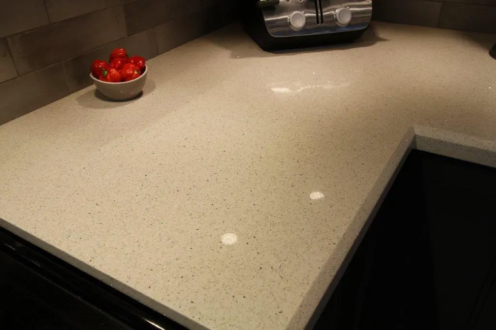 Clean beige speckled kitchen countertop with a bowl of red tomatoes and a stainless steel toaster in the background