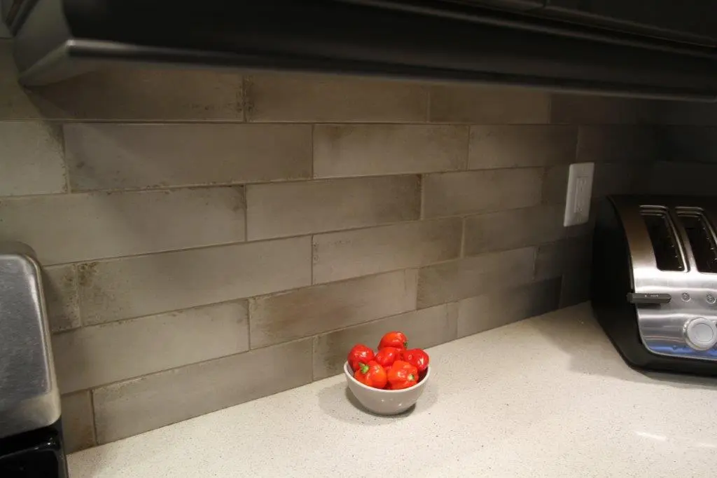 Kitchen countertop with a small white bowl filled with red peppers, a silver toaster on the right, and a tiled backsplash in shades of gray.