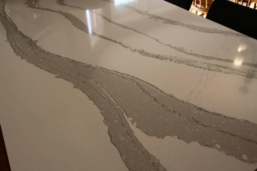 Close-up of a white marble countertop with wide grey veins and subtle speckled texture, reflecting light from above.
