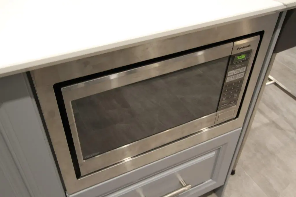 Built-in Panasonic stainless steel microwave oven installed below a white countertop with gray cabinetry and drawers beneath.