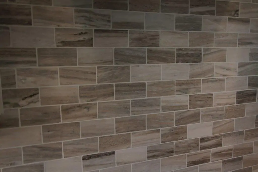 Wall covered with rectangular beige and brown tiles arranged in a staggered brick pattern with natural stone texture.
