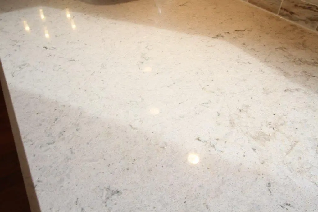 Close-up of a light-colored, polished granite countertop with subtle gray veining and reflections of overhead lights.