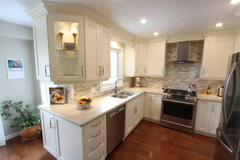 Bright modern kitchen with white cabinets, stainless steel appliances, wood flooring, a countertop with a fruit bowl and a cookbook, and a window over the sink.