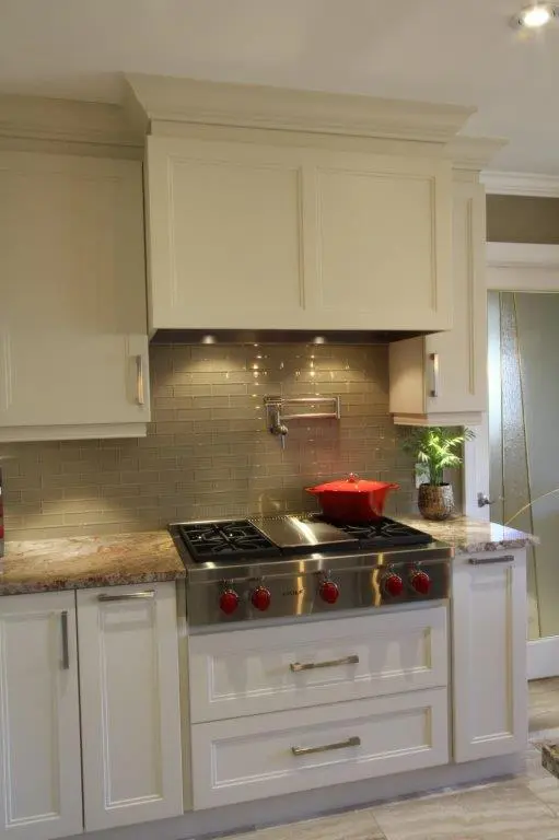 Modern kitchen with cream cabinetry, granite countertops, a stainless steel gas stove with red knobs, a red pot on the stove, a beige subway tile backsplash with under-cabinet lighting, and a small potted plant on the countertop.