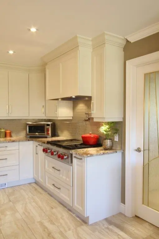 Modern kitchen corner with white cabinets, a stainless steel stove with red knobs, a red pot on the stove, a toaster oven on the countertop, beige backsplash tiles, and a glass-paneled door on the right side.