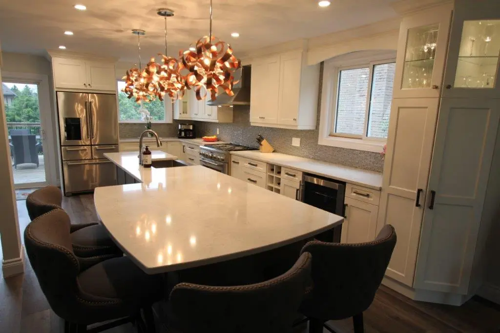 Modern kitchen with white cabinets, a large white marble island, brown upholstered chairs, stainless steel fridge, gas stove, and three artistic pendant lights hanging above the island.