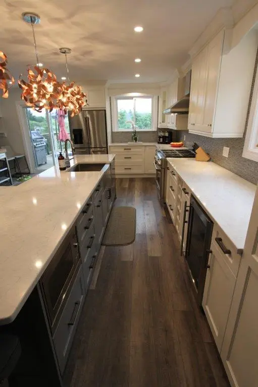 Modern kitchen with dark wooden floors, light gray island with marble countertop and built-in microwave, stainless steel appliances, white cabinetry, and two artistic pendant lights above the island.