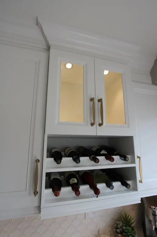 White kitchen cabinet with two glass-paneled doors above shelves holding multiple wine bottles stored horizontally.