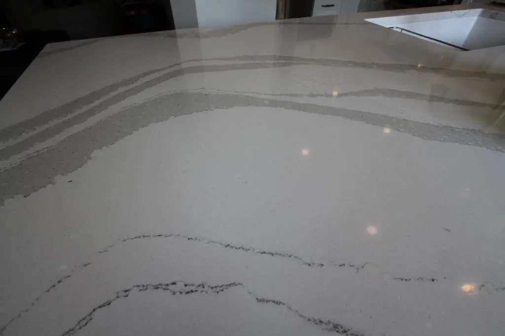 Close-up of a polished white and gray quartz countertop with natural veining and a built-in sink on the right edge under soft lighting.