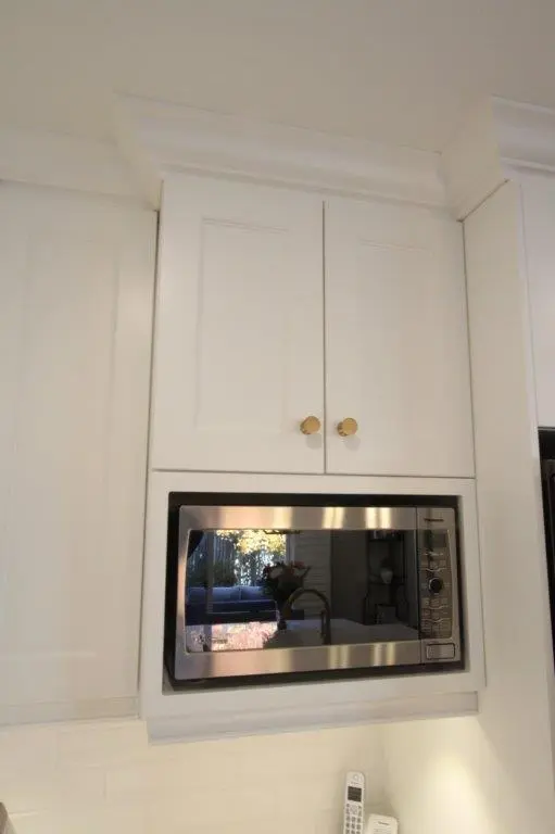 Built-in stainless steel microwave installed under white kitchen cabinets with gold knobs and white subway tile backsplash.