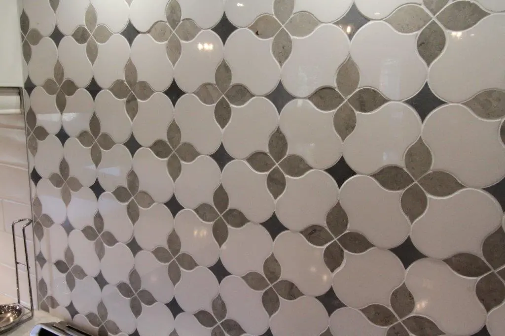 Kitchen backsplash with decorative tiles featuring a repeating pattern of cream-colored shapes with gray centers arranged in a floral-like design.