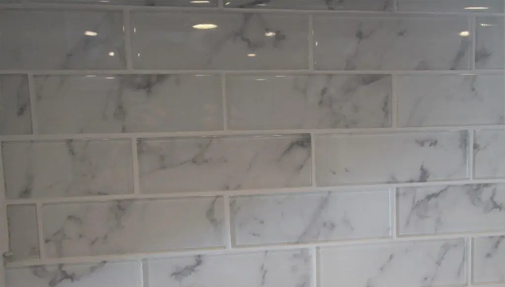 Close-up of glossy white subway tiles with gray marbled patterns and grout lines between them