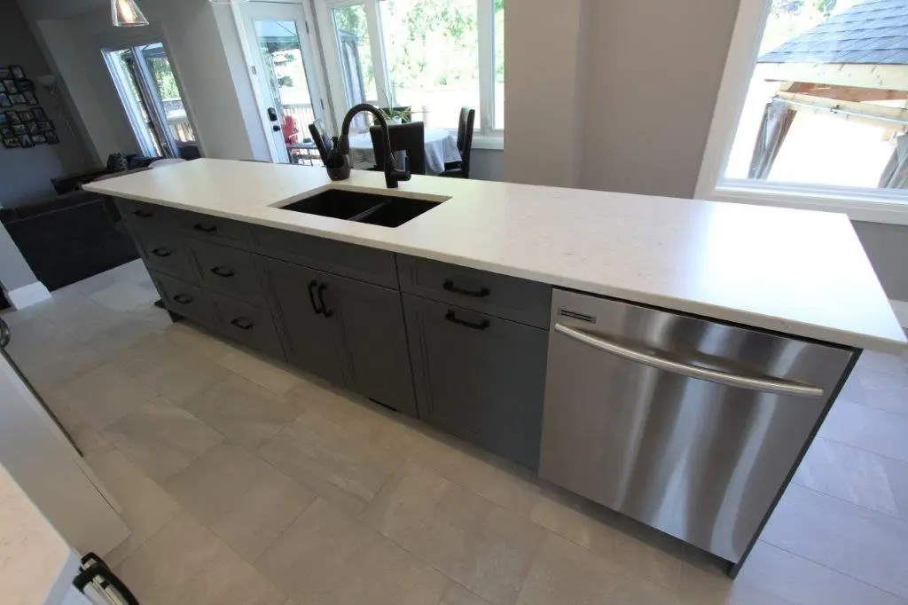 Modern kitchen island with white countertop, dark gray cabinets, a black sink and faucet, and a stainless steel dishwasher under large windows.