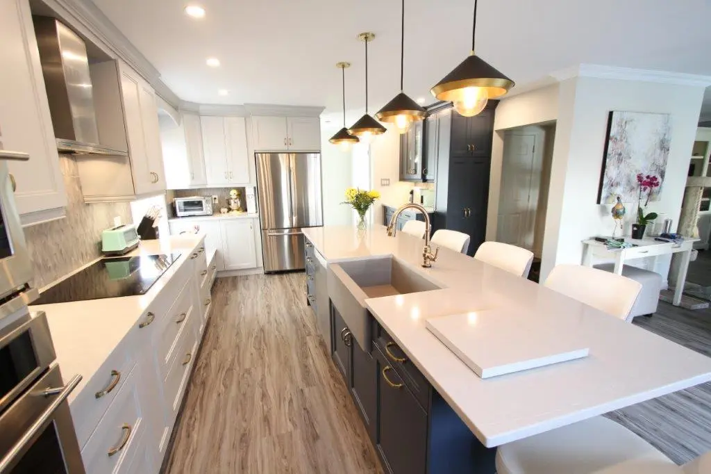 Modern kitchen with white countertops and cabinetry, a large island with dark blue cabinets, three pendant lights, stainless steel appliances, and wood-look flooring