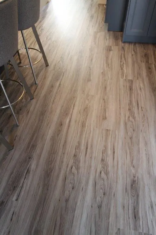 Close-up view of a light brown wood laminate floor in a kitchen area with part of gray bar stools and gray cabinetry visible.