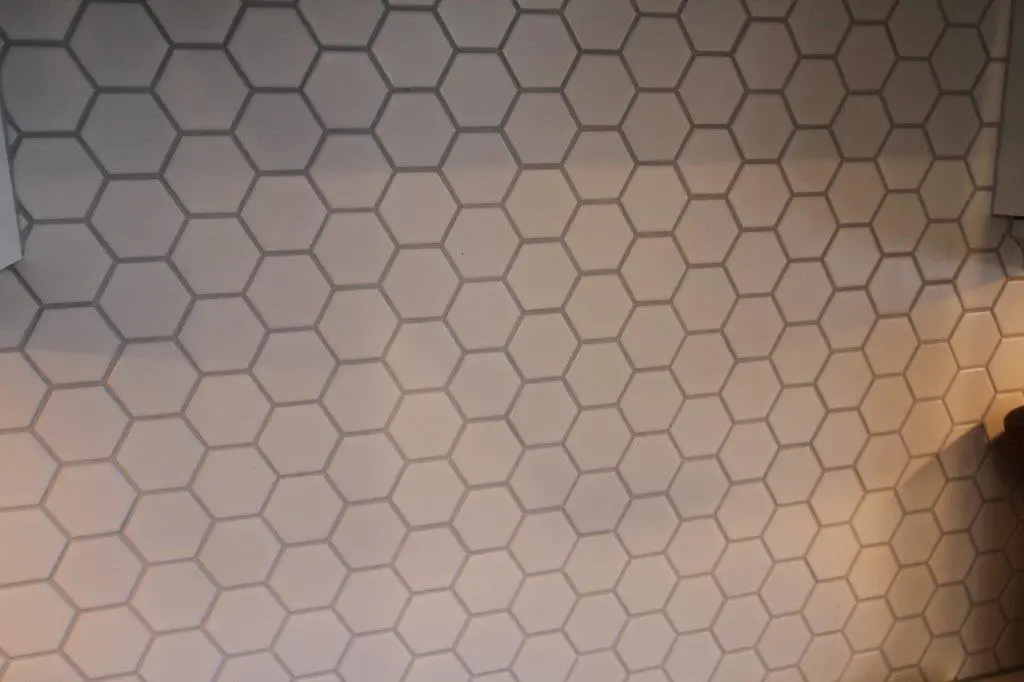 Close-up view of a wall covered with beige hexagonal tiles with grout lines in between, showing a geometric honeycomb pattern