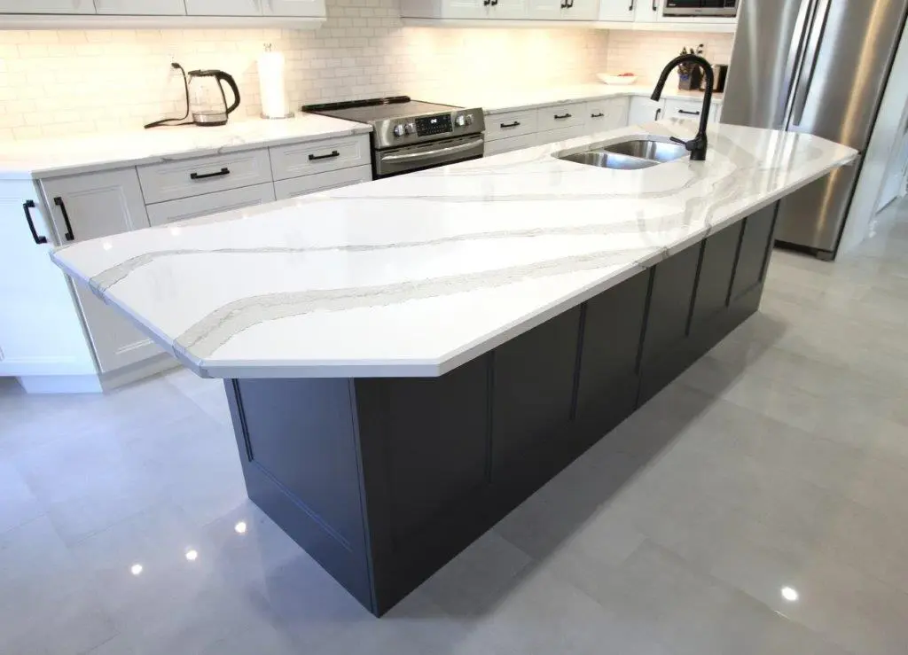 Modern kitchen with a large white island countertop featuring gray veining, dark gray base cabinets, a dual sink, and a black faucet, with white upper and lower cabinetry, stainless steel appliances, and bright lighting.