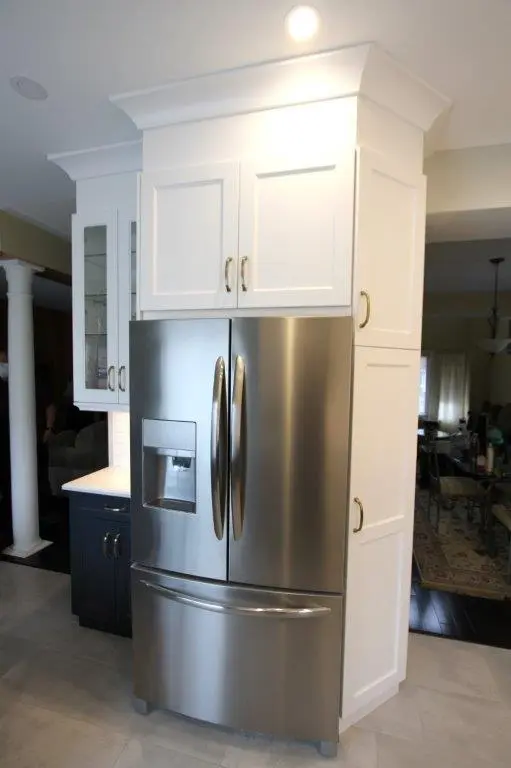 Stainless steel French door refrigerator with water dispenser, surrounded by white cabinetry with gold handles in a modern kitchen.