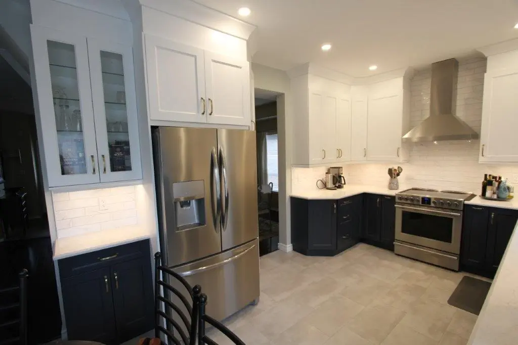 Modern kitchen with white upper cabinets and dark lower cabinets, stainless steel refrigerator with water dispenser, stainless steel stove with range hood, white subway tile backsplash, coffee maker on counter, and gray tiled floor.
