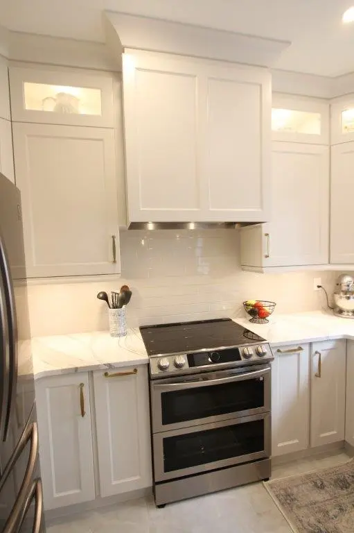 Modern kitchen with white cabinetry, a stainless steel double oven stove with black cooktop, white tiled backsplash, quartz countertops, a utensil holder, a fruit basket, and a silver stand mixer on the counter.