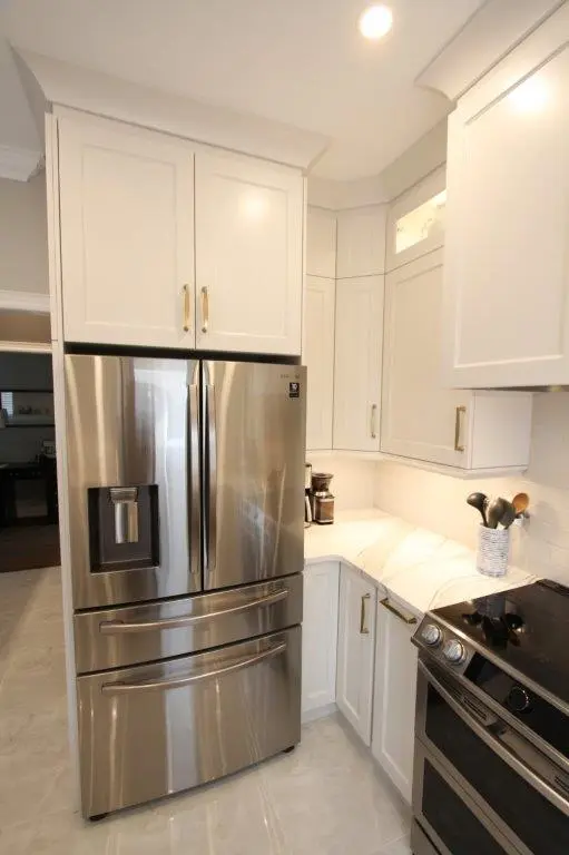 Modern kitchen corner featuring a stainless steel French door refrigerator with water dispenser, white cabinetry with gold handles, quartz countertops, a coffee maker, and a black electric stove.