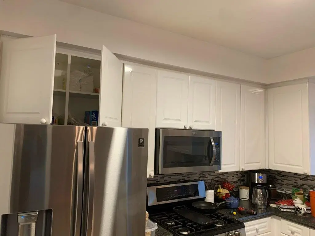 A before picture of a Kitchen with stainless steel refrigerator with partially open upper cabinets, a stainless steel microwave above a gas stove, a coffee maker on the counter, various kitchen items and a tiled backsplash.