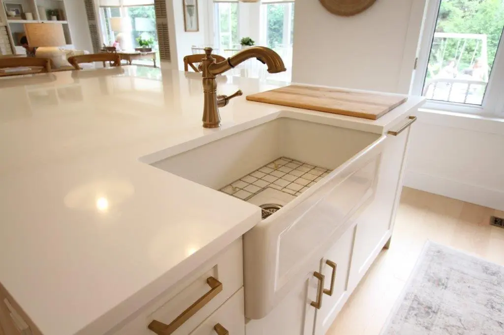 Modern kitchen sink with a large white countertop, gold faucet, and an integrated wooden cutting board next to a window.