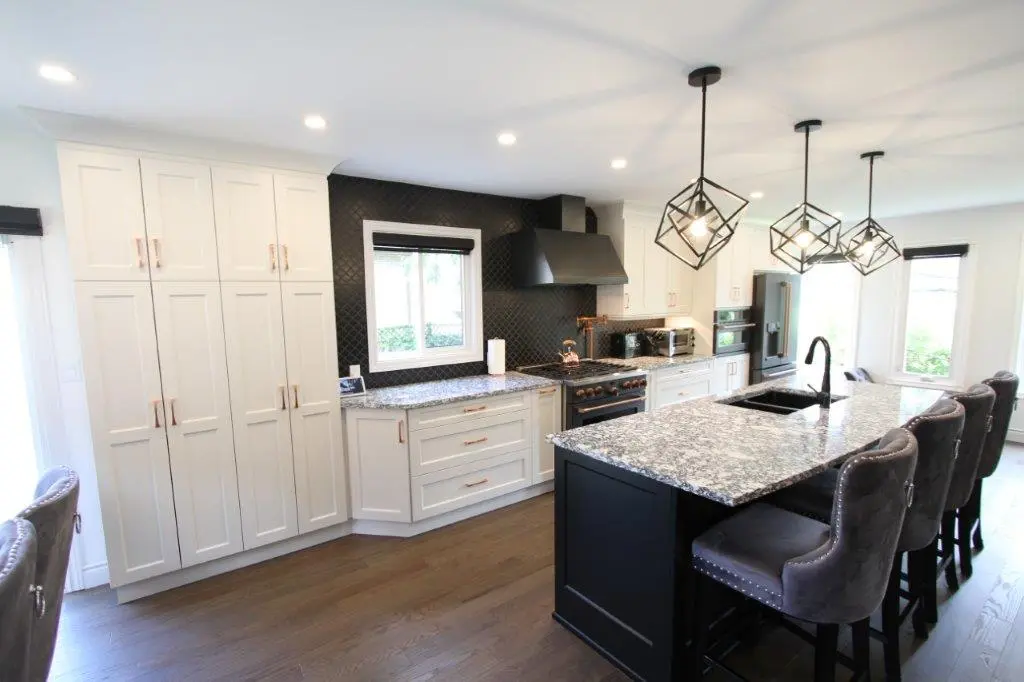 Modern kitchen with white cabinets, a black range hood, quartz countertops, and an island with bar stools. Three geometric pendant lights hang above the island, and there is a large window by the sink area.