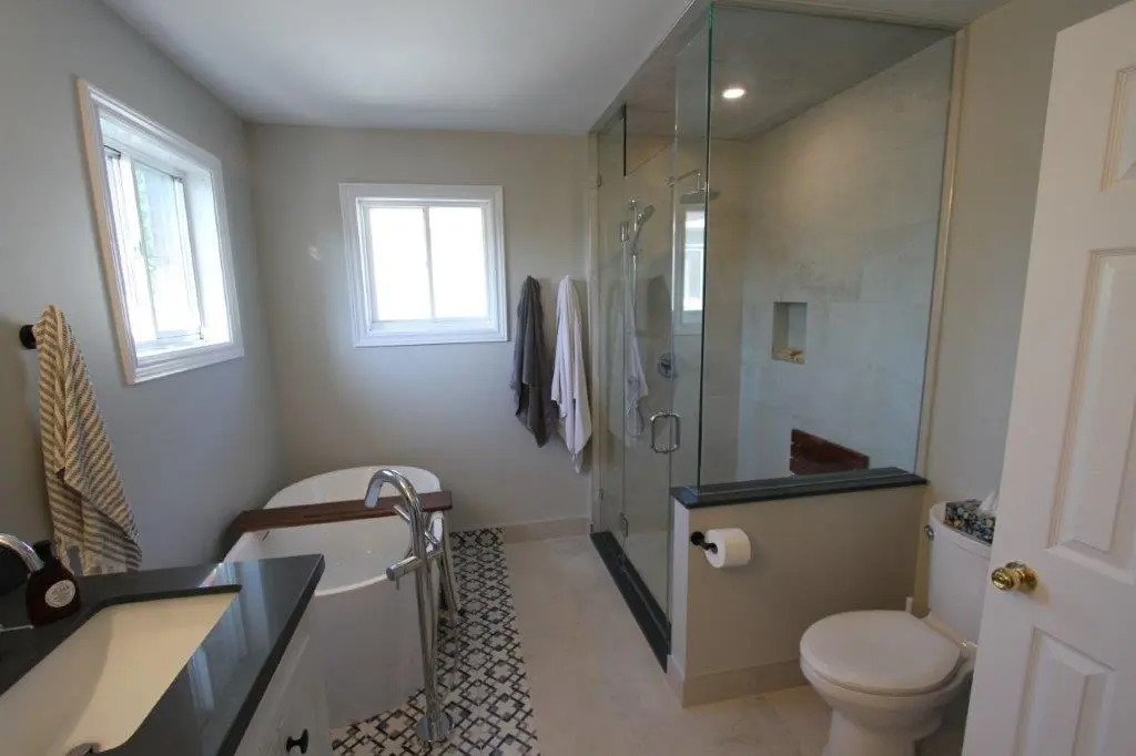 Modern bathroom with a freestanding bathtub, glass-enclosed shower, toilet, and a vanity with a sink, featuring light-colored walls and floor tiles.