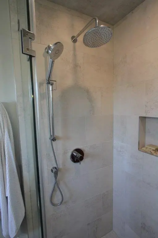 A modern shower with a rain showerhead and handheld shower attachment in a tiled enclosure with a built-in shelf.