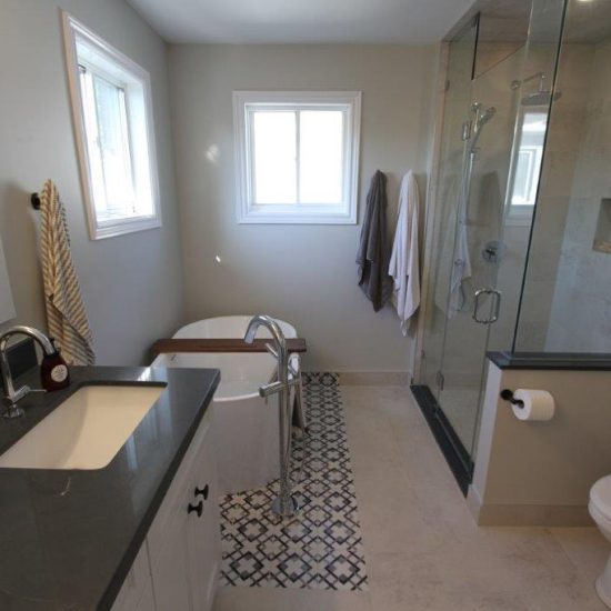Modern bathroom with a dark countertop and sink on the left, freestanding bathtub in the center, and a glass-enclosed shower on the right, next to the toilet.