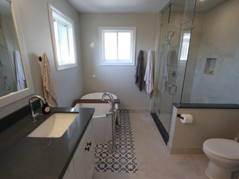 Modern bathroom with a dark countertop and sink on the left, freestanding bathtub in the center, and a glass-enclosed shower on the right, next to the toilet.