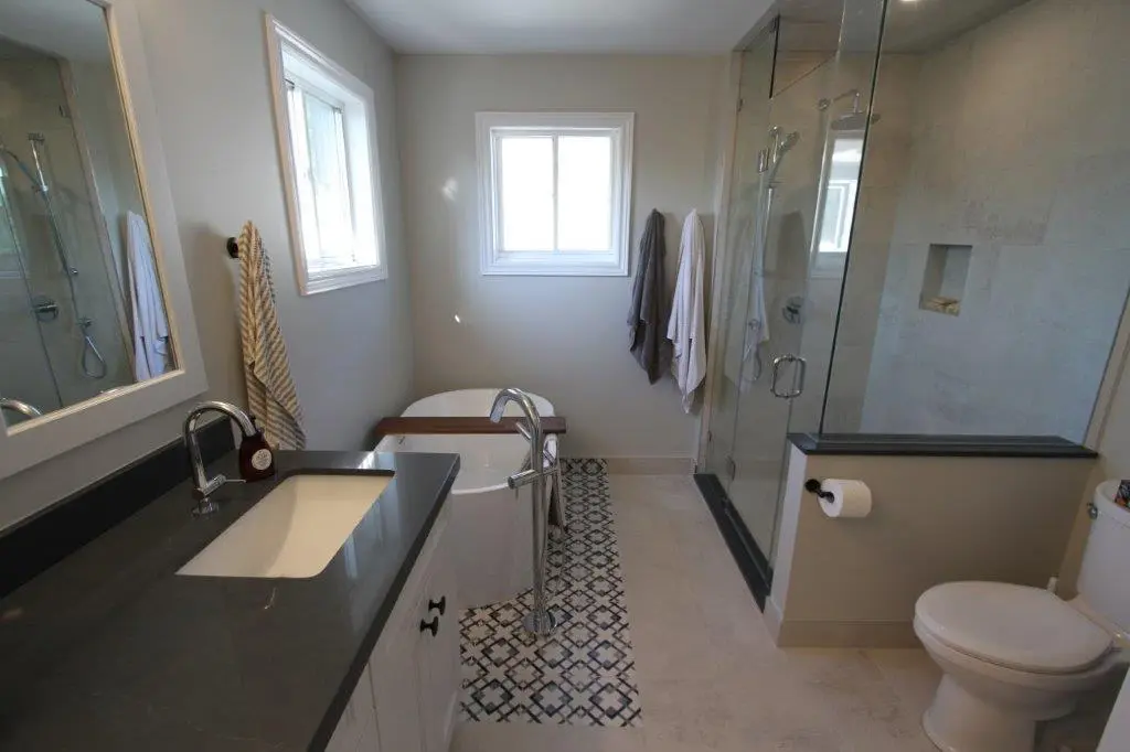 Modern bathroom with a dark countertop and sink on the left, freestanding bathtub in the center, and a glass-enclosed shower on the right, next to the toilet.