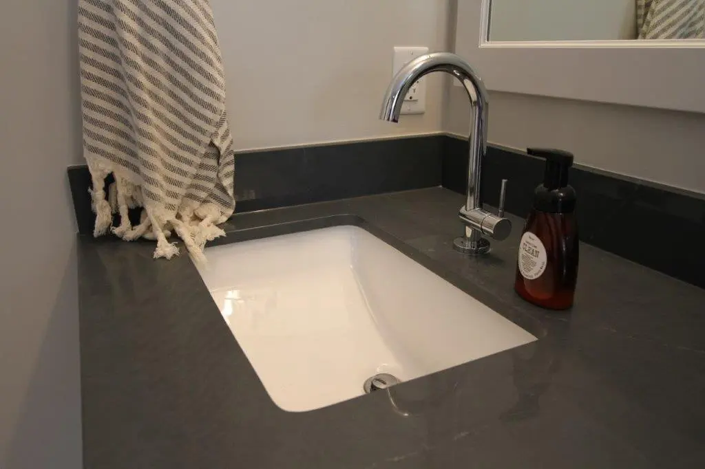 A modern bathroom sink with a shiny chrome faucet, accompanied by a striped towel hanging to the side and a bottle of hand soap on the countertop.