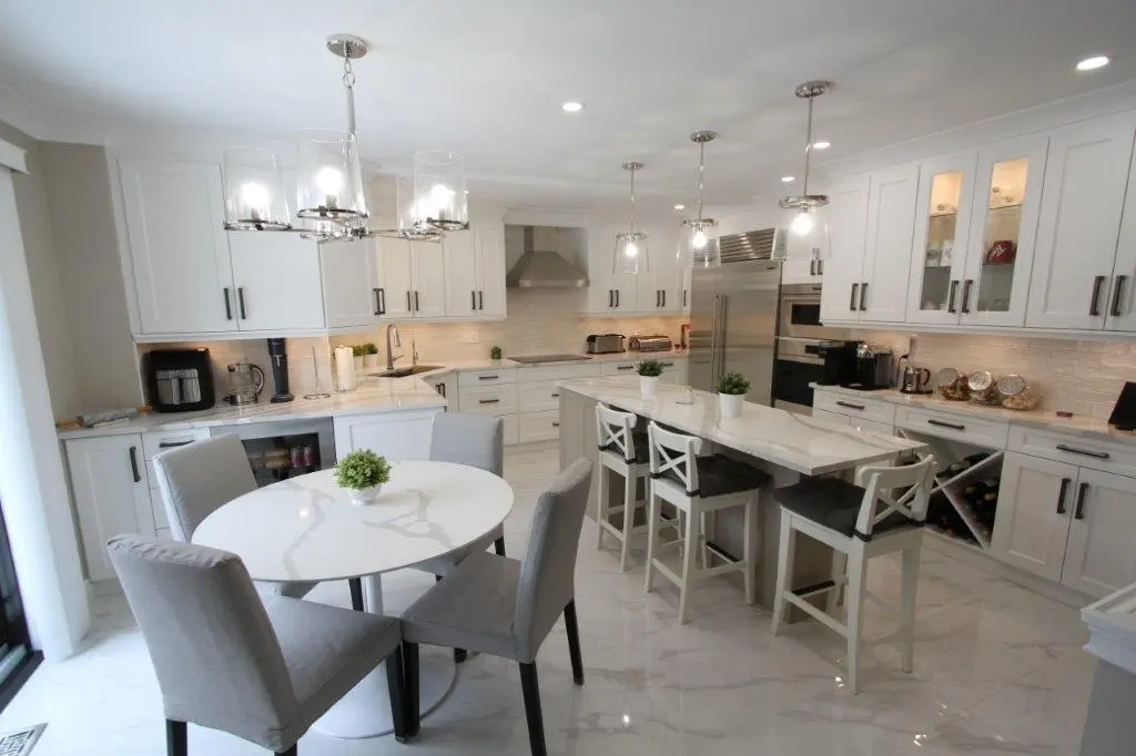 Modern kitchen with white cabinetry, a large island with bar stools, a round dining table with gray chairs, and stainless steel appliances.